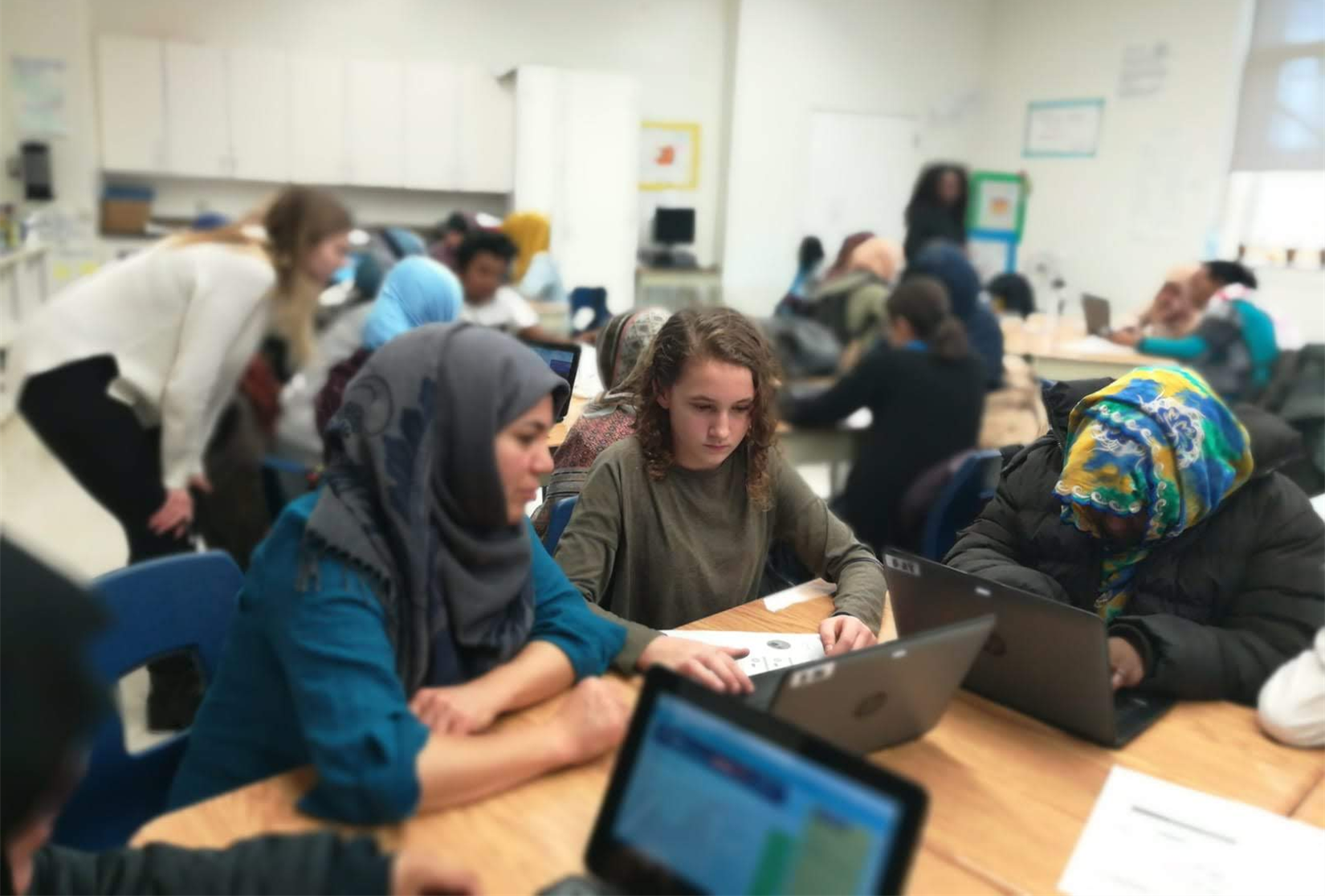 A YEP session in a classroom: youth tutors teaching adult learners at laptops while two coaches watch and help