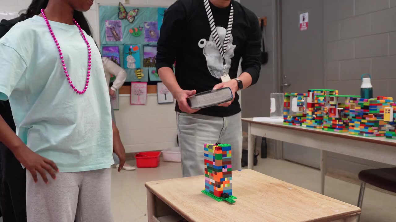 A volunteer and children testing a colourful Lego tower in a classroom