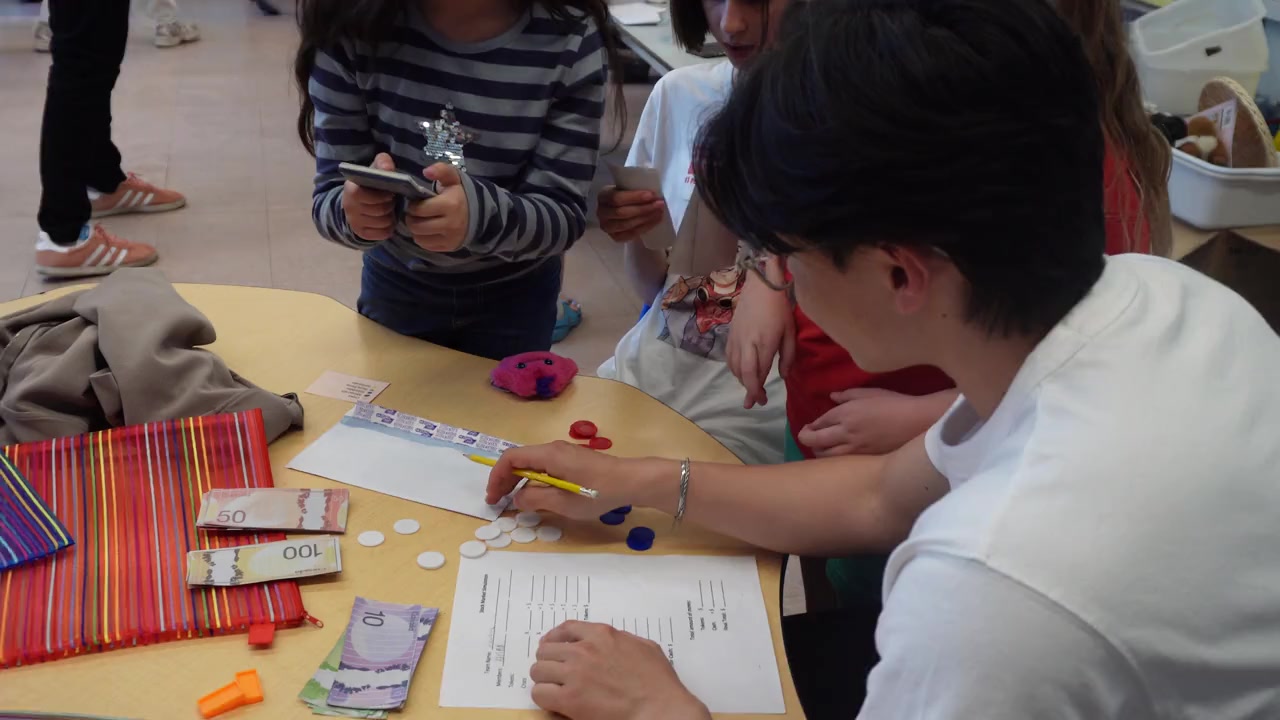 Children and a volunteer using play money during a financial literacy activity
