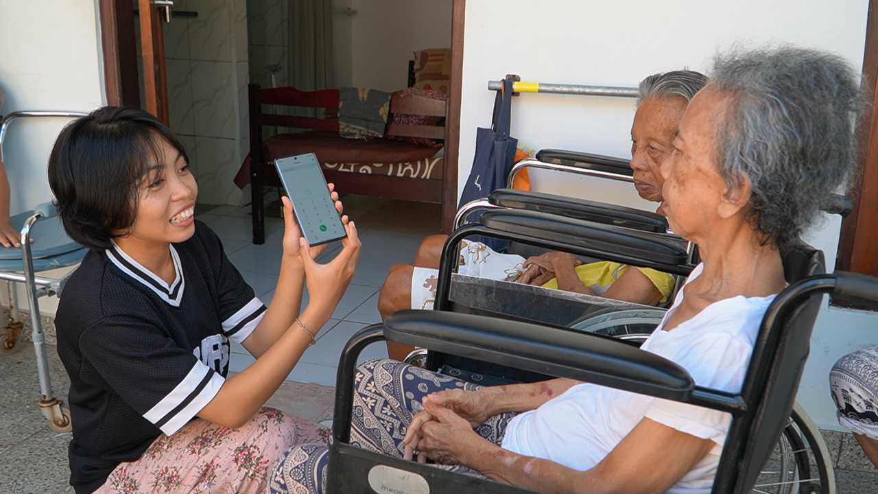 A young woman in Indonesia showing two seniors in wheelchairs how to use a phone